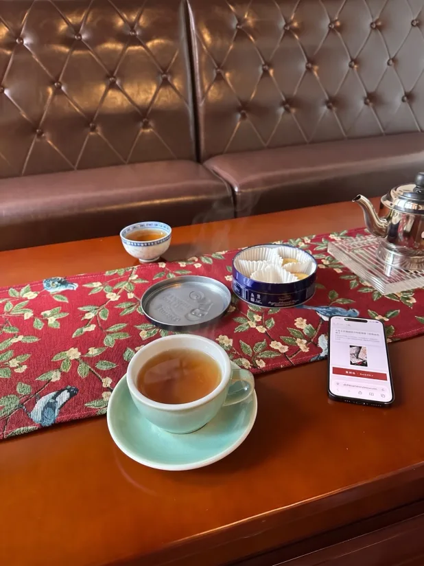 茶樓卡座嘅枱面:一杯熱茶、一個蓋碗、一罐餅,同一部擺喺枱上面嘅電話